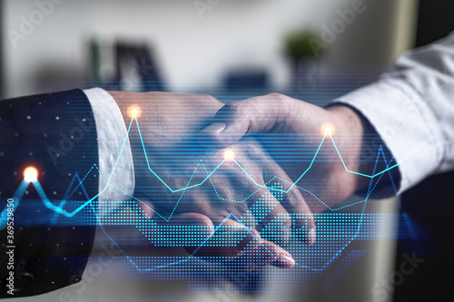 Double exposure of two businesspeople handshake and financial chart hologram drawing background. Concept of partnership in business and data analysis. Formal wear.