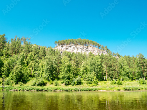 Nature, river, mountains, forests on a summer day against the blue sky. Rocky shore with the forest.