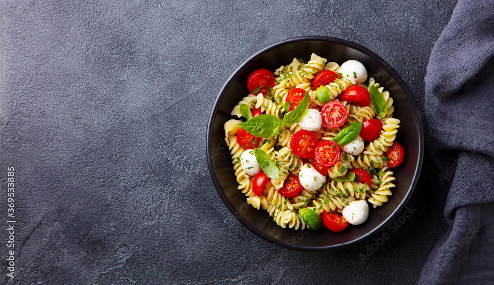 Pasta fusilli with mozzarella cheese, tomatoes and basil. Dark background. Copy space. Top view. Pasta fusilli with mozzarella cheese, tomatoes and basil. Dark background. Copy space. Top view.