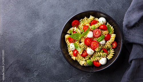 Pasta fusilli with mozzarella cheese, tomatoes and basil. Dark background. Copy space. Top view.