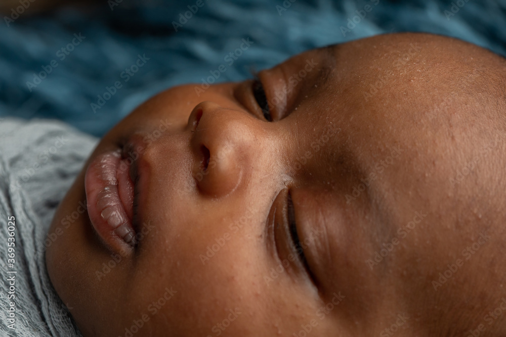 Close-up sleepy swaddled African-American newborn baby boy laying on a blue rug in a basket with copy space Close-up sleepy swaddled African-American newborn baby boy laying on a blue rug in a basket with copy space