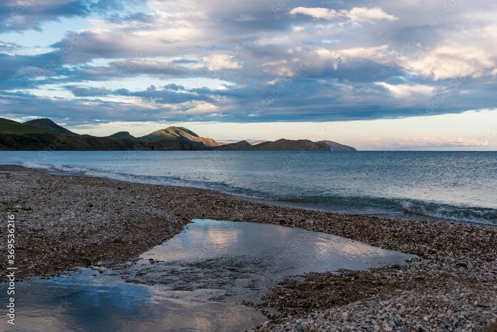 Deserted pebble beach against the backdrop of mountains at sunset