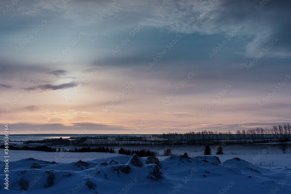 Winter sunrise in a field with snowy bumps and a river in the background