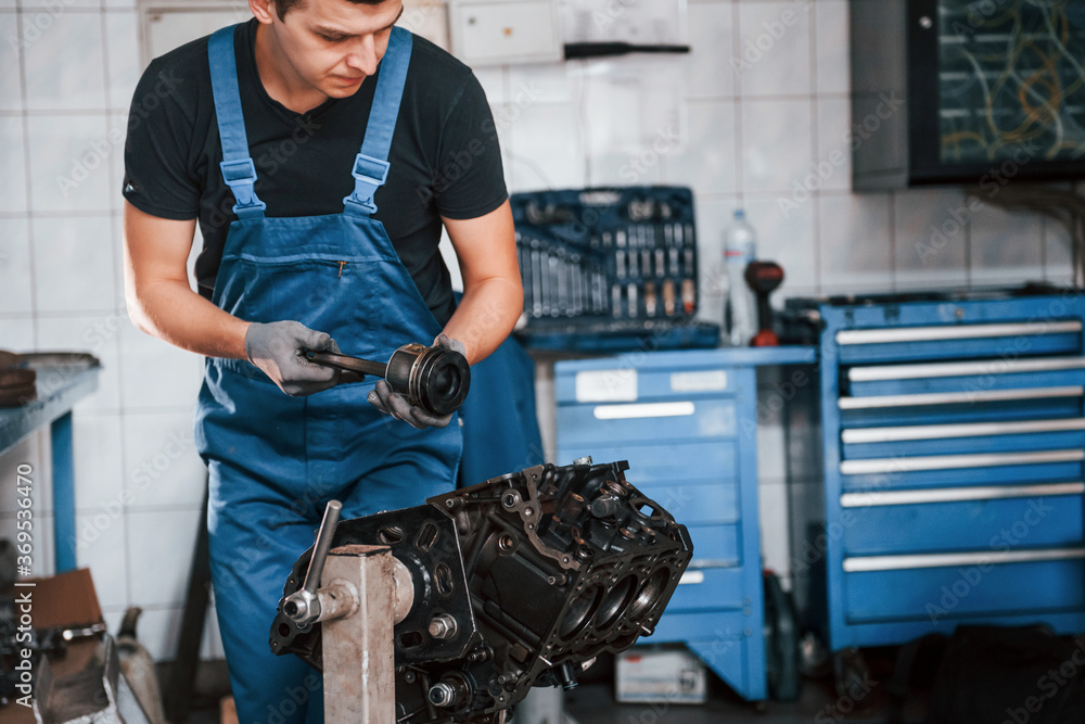Professional repairman in garage works with broken automobile engine Professional repairman in garage works with broken automobile engine