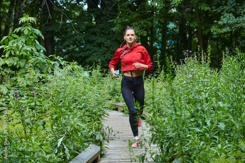 Attractive girl in sportswear jogging along a wooden path in a forest park.