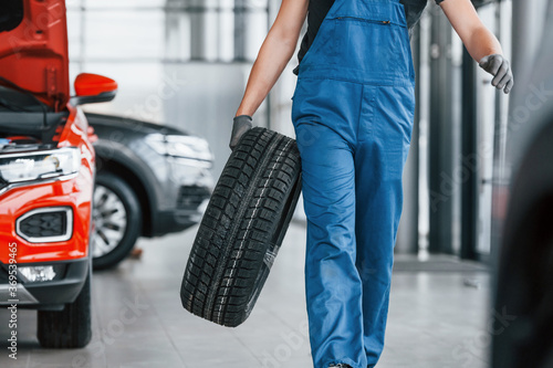 Worker in black and blue uniform holding car wheel and have job indoors