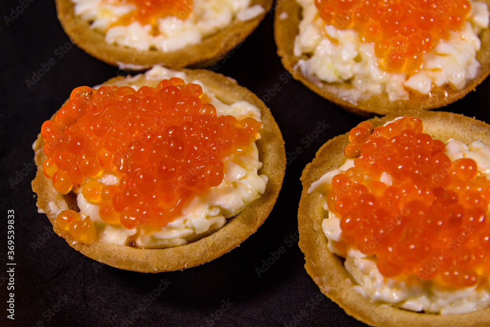Tartlets with red caviar on a black plate. Festive food