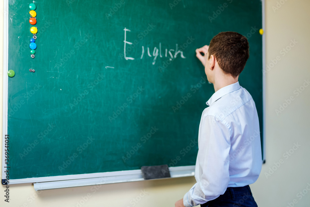 Schoolboy in light shirt wrting english words on blackboard. Back to school concept. Schoolboy in light shirt wrting english words on blackboard. Back to school concept.