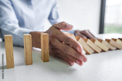 business woman hand stopping wooden block from falling the line of domino