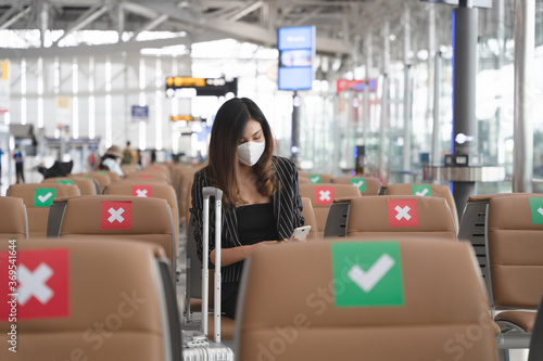 Asian Business woman wearing face mask talking on the phone while sitting on the chair that marked with Social distancing sticker, New normal concept of society with social distancing for public place