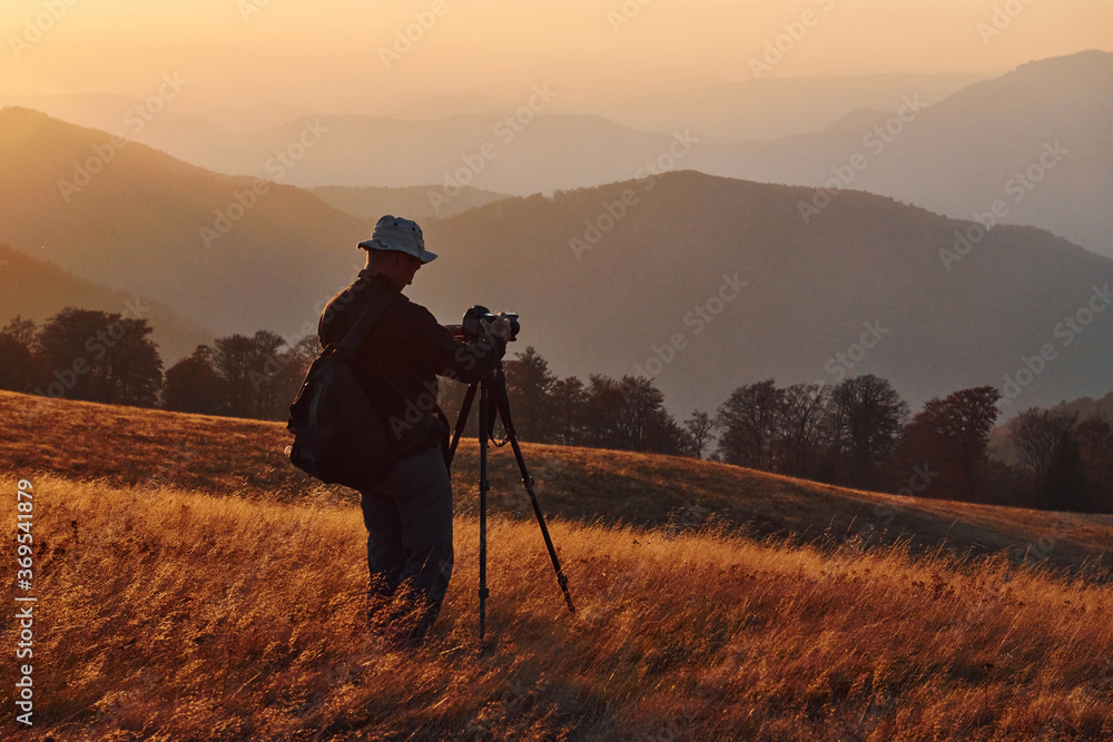 Male photographer standing and working at majestic landscape of autumn trees and mountains by the horizon