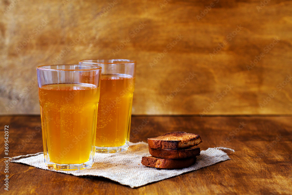 Summer soft drink. Two glass of homemade bread kvass with copy space. Beer with sackcloth on a wooden table with black rye bread hard chucks. Summer soft drink. Two glass of homemade bread kvass with copy space. Beer with sackcloth on a wooden table with black rye bread hard chucks.