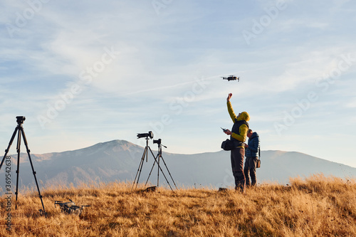 Male photographers standing and working at majestic landscape of autumn trees and mountains by the horizon