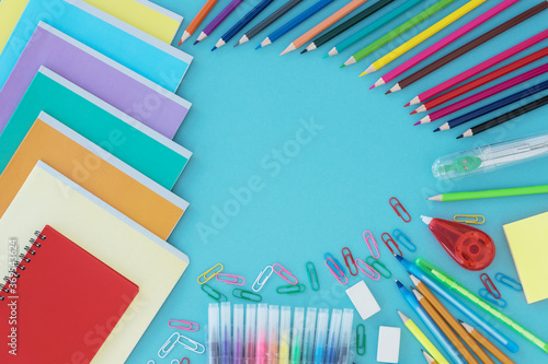 Top view of school supplies as noteboks, pencils, corrector, pens paper clips  lie on blue background. Copy space for text in middle of image. Back to school concept. photo