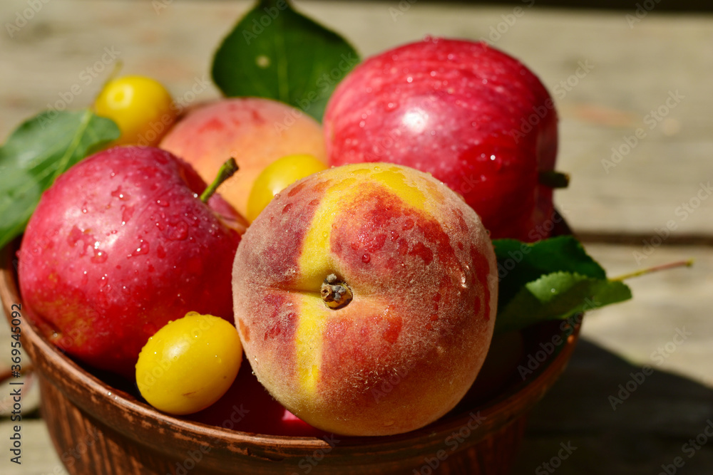 Close-up shot of juicy peaches, apples and cherry plums lie in a brown ceramic plate on a wooden table. Close-up shot of juicy peaches, apples and cherry plums lie in a brown ceramic plate on a wooden table.
