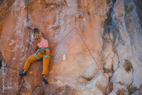 A strong woman climbs a beautiful orange rock.