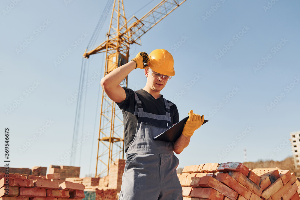 Holds notepad with documents. Construction worker in uniform and safety equipment have job on building Holds notepad with documents. Construction worker in uniform and safety equipment have job on building