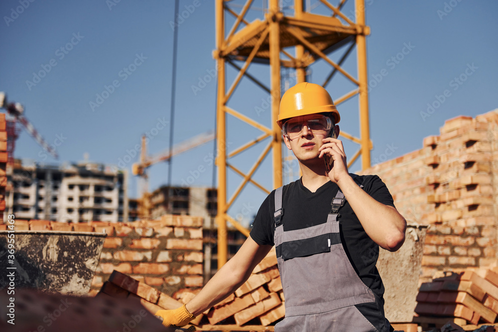 Talking by phone. Construction worker in uniform and safety equipment have job on building Talking by phone. Construction worker in uniform and safety equipment have job on building