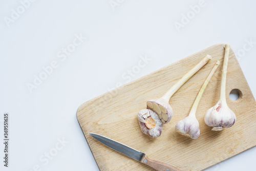 top view of garlic on wooden chopping board with knife on white background