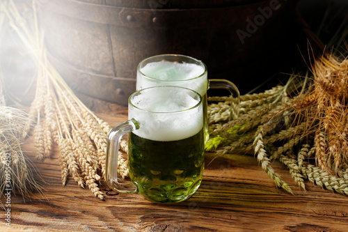 Green beers on a wooden table, in the back of the original oak barrel and wheat cob. This beer is traditionally served on St. Patrick's Day, or also during Easter times in Europe.