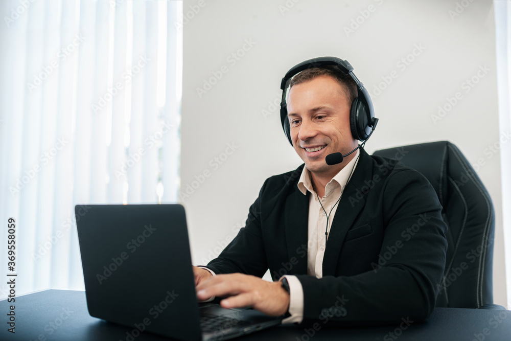 A smiling man with headphones knocks on his laptop. A smiling man with headphones knocks on his laptop.