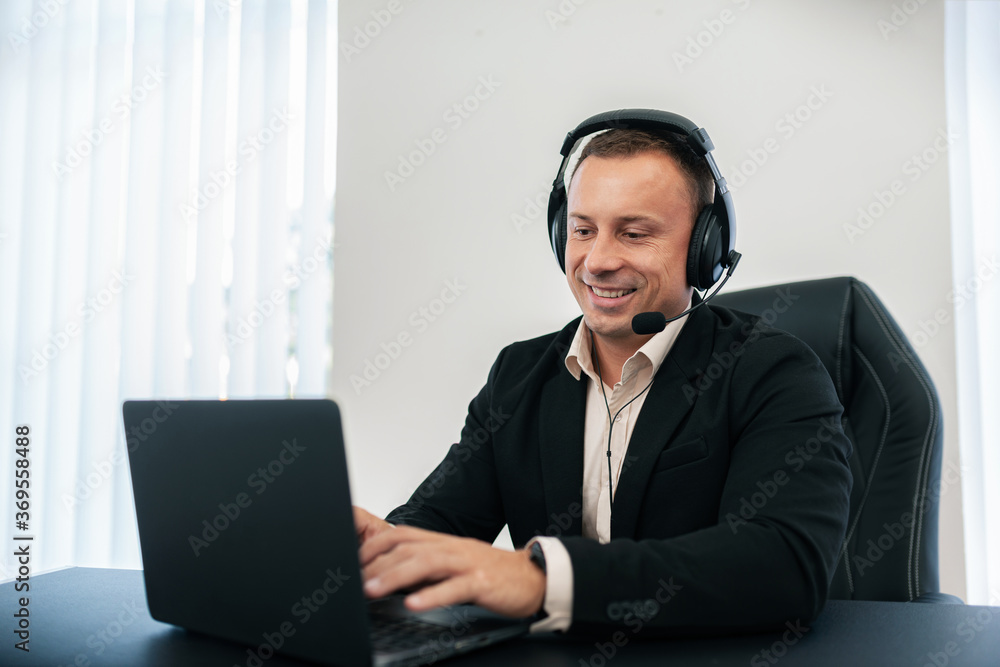 A man works happily on a laptop with headphones. A man works happily on a laptop with headphones.