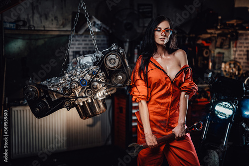Brave and very sexy looking young woman posing with a big wrench, surrounded by motorcycle details and with a motorbike on the background
