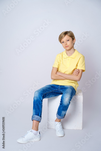 guy in yellow t shirt and blue jeans on white background is sitting on a cube