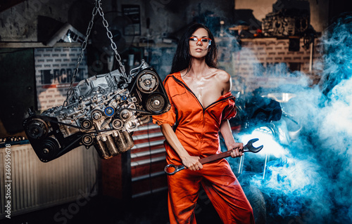 Sexy woman in safety googles and orange work jumpsuit posing with a wrench in her hands