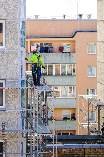 the worker assembles the scaffolding on the facade of a multi-storey house at a dangerous height © Zigmunds