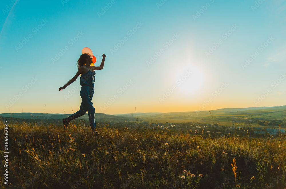 Silhouette of a young woman running with balloons on a hill backlit by sunset golden light, concept of freedom and carelessness Silhouette of a young woman running with balloons on a hill backlit by sunset golden light, concept of freedom and carelessness