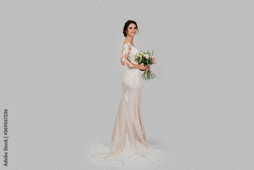 Young attractive bride with bouquet in modern bridal look with cap sleeves and an illusion neckline top off the column silhouette and sweeping train. Bride girl in studio on white background Young attractive bride with bouquet in modern bridal look with cap sleeves and an illusion neckline top off the column silhouette and sweeping train. Bride girl in studio on white background