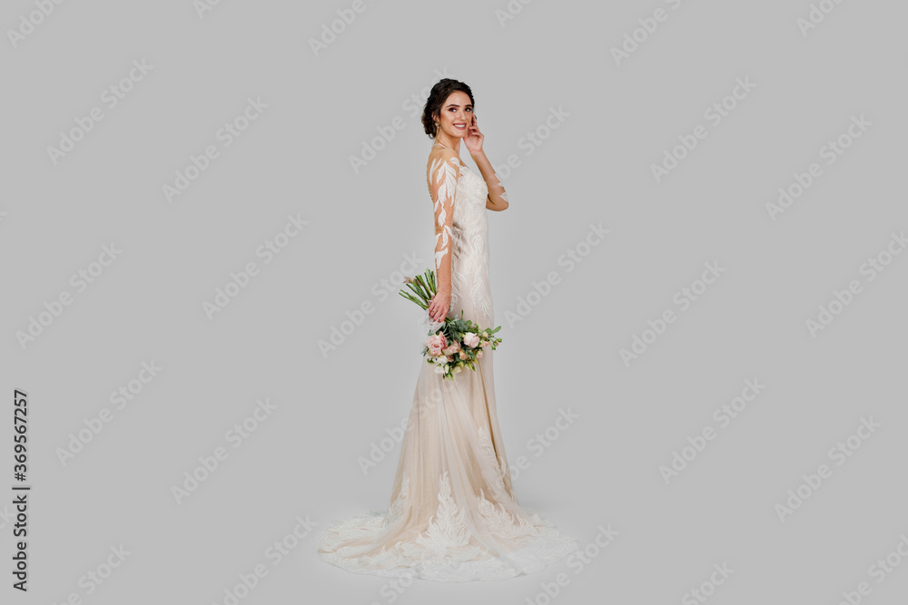 Young attractive bride with bouquet in modern bridal look with cap sleeves and an illusion neckline top off the column silhouette and sweeping train. Bride girl in studio on white background Young attractive bride with bouquet in modern bridal look with cap sleeves and an illusion neckline top off the column silhouette and sweeping train. Bride girl in studio on white background