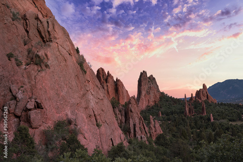 Garden of the Gods with colorful pink and purple sunset. Beautiful colors cast light on the rock formations in colorado springs. Colorful clouds, green trees, and orange rocks visible