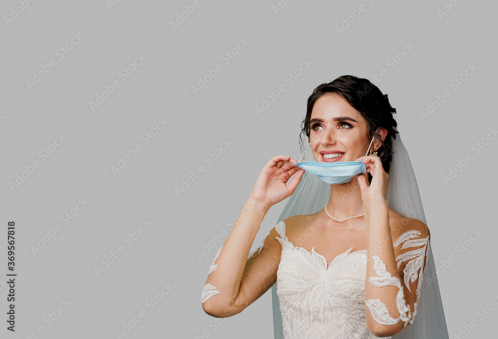Bride in medical mask and wedding bouquet at coronavirus covid-19 quarantine period. Attractive girl takes off mask and looks left side with blank place on white background Bride in medical mask and wedding bouquet at coronavirus covid-19 quarantine period. Attractive girl takes off mask and looks left side with blank place on white background