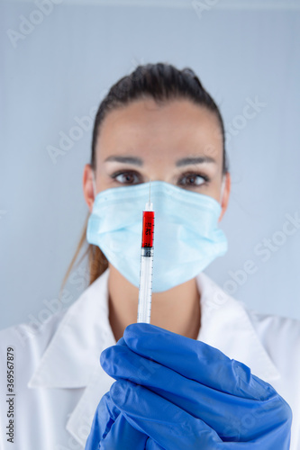 Attractive female doctor with virus protection mask and latex gloves carrying a syringe of the sars2 covid19 coronavirus vaccine photo