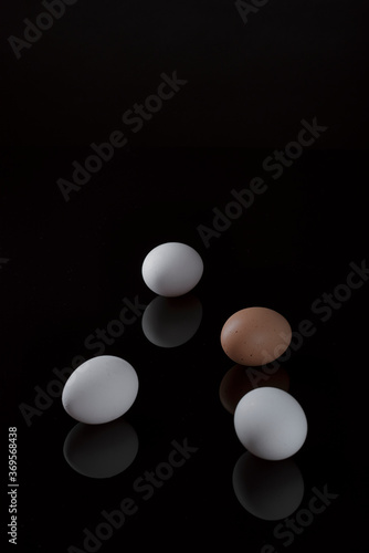 drei weiße Eier und ein braunes Ei auf schwarzer reflektierender Oberfläche