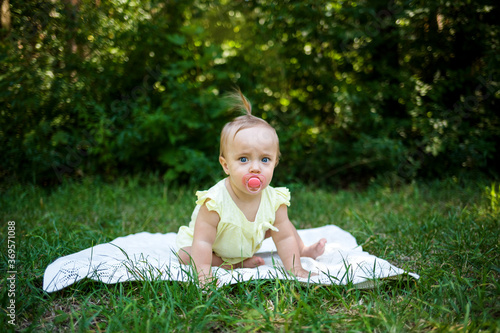 a little girl with a pacifier is on all fours on a blanket in nature