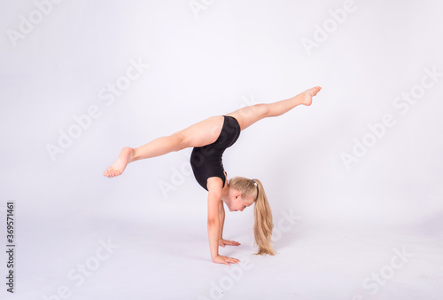 a blonde gymnast in a black swimsuit performs splits on her hands on a white isolated background with space for text
