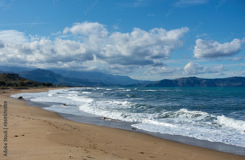 Scenic view of waves hitting the sandy shore at Episkopi Beach, Crete, Greece, with distant mountains under a blue sky filled with dramatic clouds Scenic view of waves hitting the sandy shore at Episkopi Beach, Crete, Greece, with distant mountains under a blue sky filled with dramatic clouds