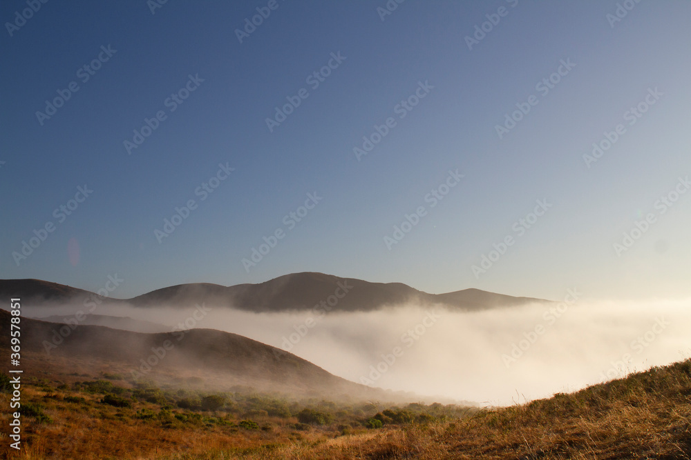 Misty clouds cover distant mountains with fog. Looking east in the morning from Point Mugu State Park's trail. Misty clouds cover distant mountains with fog. Looking east in the morning from Point Mugu State Park's trail.
