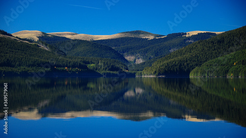 Vidra lake - afternoon autumn reflection of the Lotru Mountains into the calm lake waters. Carpathia, Romania.