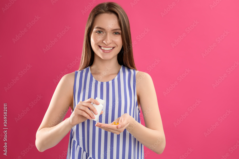 Young woman with bottle of vitamin pills on pink background