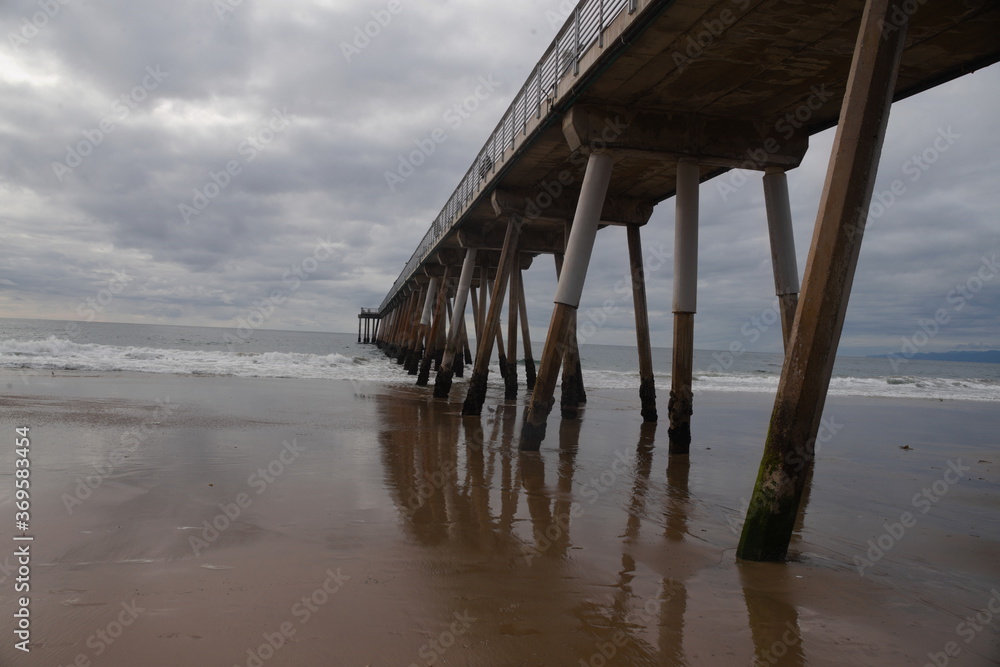 Leading lines of beach pier extending out into the pacific ocean on a cloudy and threatening day.. Communicate gloom, repeating pattern, boredom, lack of things to do, isolation, movement of earth. 