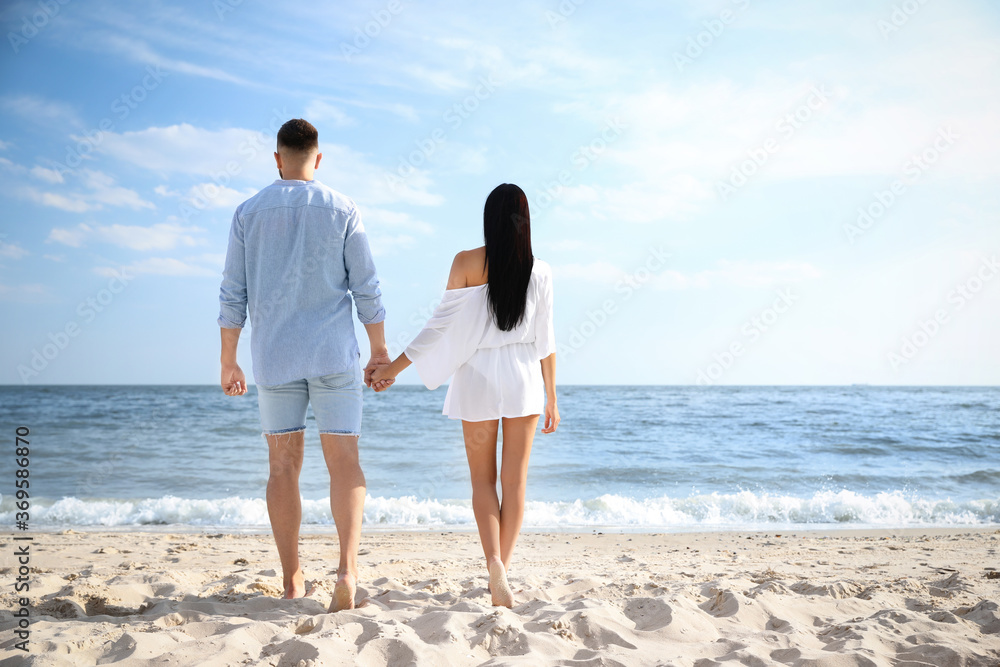 Lovely young couple walking together on beach, back view Lovely young couple walking together on beach, back view