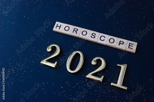 Word Horoscope and numbers 2021. Wooden blocks with lettering on dark blue background decorated with golden glitters. Selective focus.