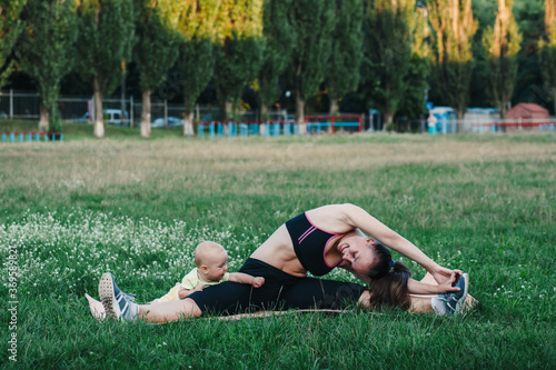 woman mom sits on the grass in nature and does stretching warm-up, next to her baby crawls