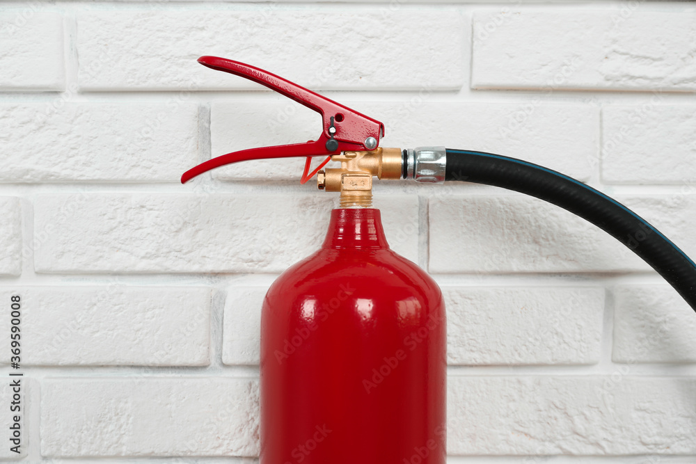 Naklejka premium Fire extinguisher near white brick wall, closeup