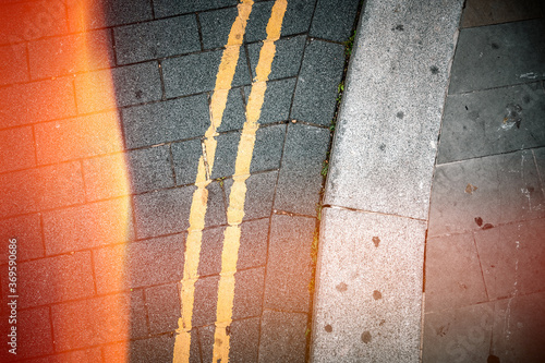 double yellow lines on grey road next to pavement with summer light leak shining in from the sider photo