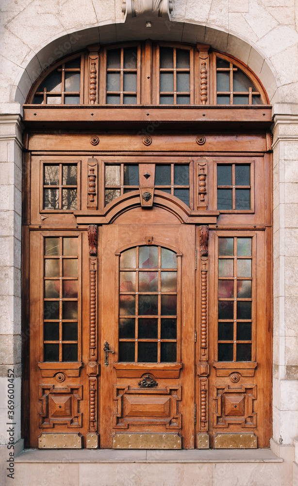 A huge old carved brown door with glass inserts on the facade of the building.